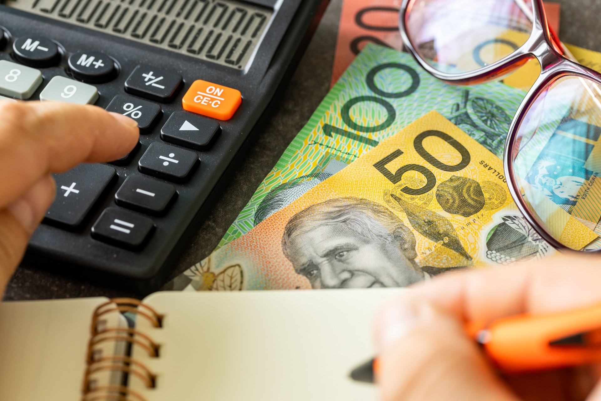Australia money, financial analysis, company accounting, tax calculation, financial business concept. Australian dollars together with a calculator, hand writing down the results in a notebook